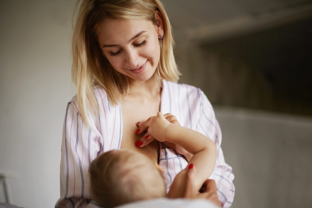 Agosto Dourado é o mês de conscientização sobre a amamentação 1 back view of adorable six month old infant drinking breast milk attractive young european woman in home clothing cradling her baby daughter in arms breastfeeding her enjoying deep connection